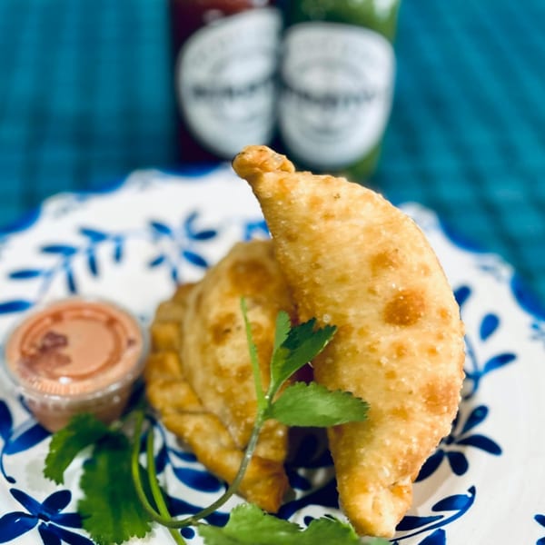 Two golden-brown empanadas with cilantro and dipping sauce on a white and blue plate.