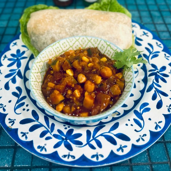 A burrito with lettuce and a side of chunky salsa with corn and cilantro on a blue and white plate.