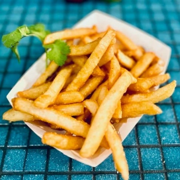 Golden french fries in a white paper tray, garnished with cilantro on a blue tiled surface.