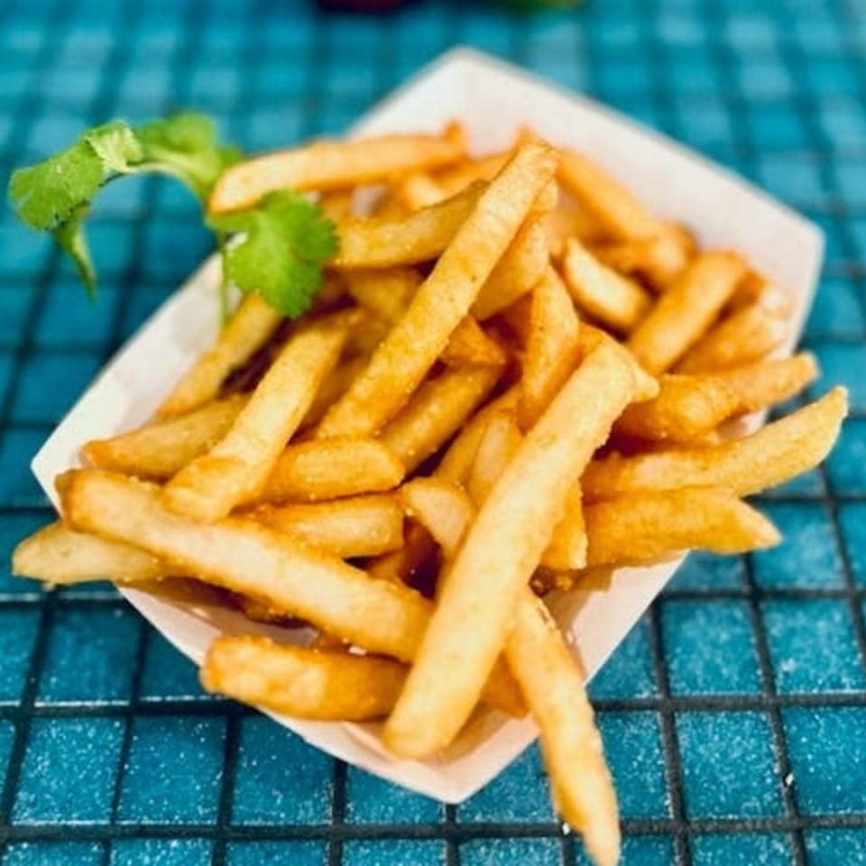 Golden french fries in a white paper tray, garnished with cilantro on a blue tiled surface.