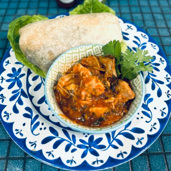 A burrito and a bowl of stewed meat in red sauce, garnished with cilantro, on a blue and white plate.