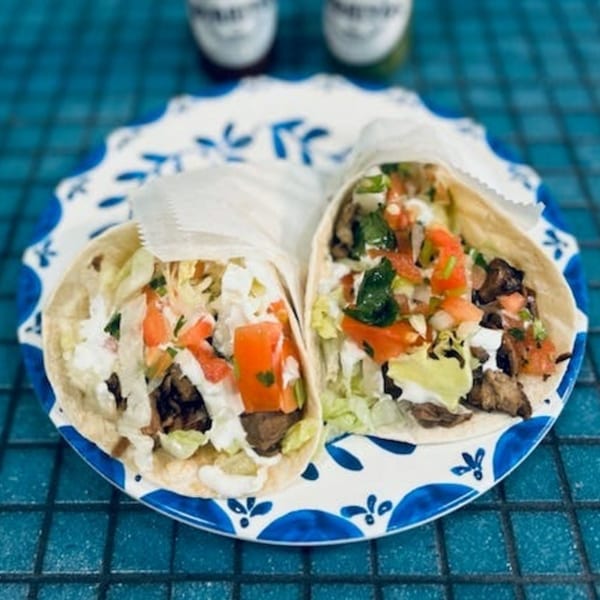 Two tacos with meat, lettuce, tomato, and sour cream on a blue and white plate.