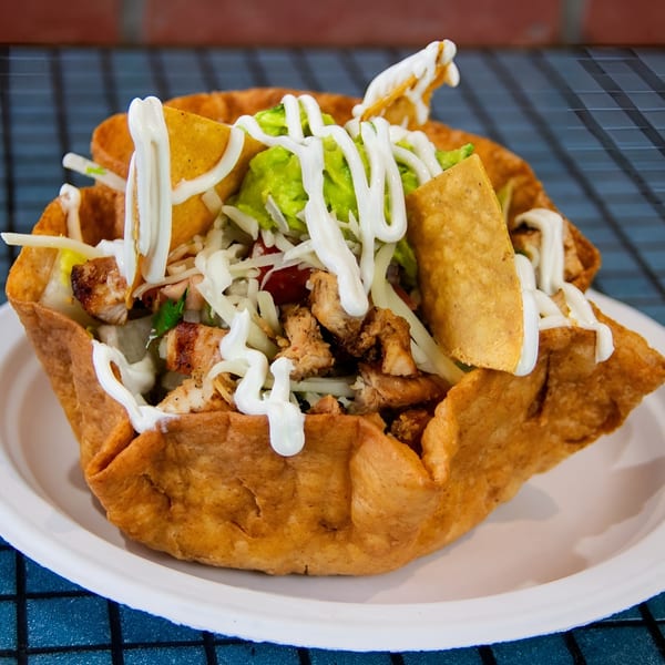 Chicken taco salad in a crispy tortilla bowl, topped with guacamole, cheese, and sour cream.