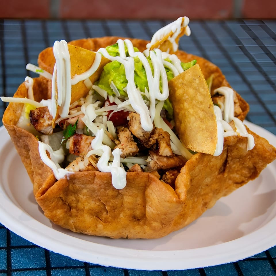 Chicken taco salad in a crispy tortilla bowl, topped with guacamole, cheese, and sour cream.